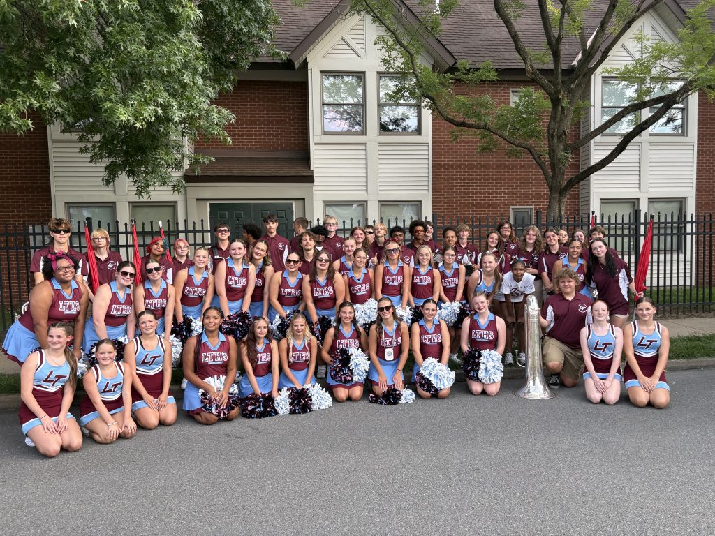 Members of the marching band, cheerleading team and color guard stand for a group photo downtown.